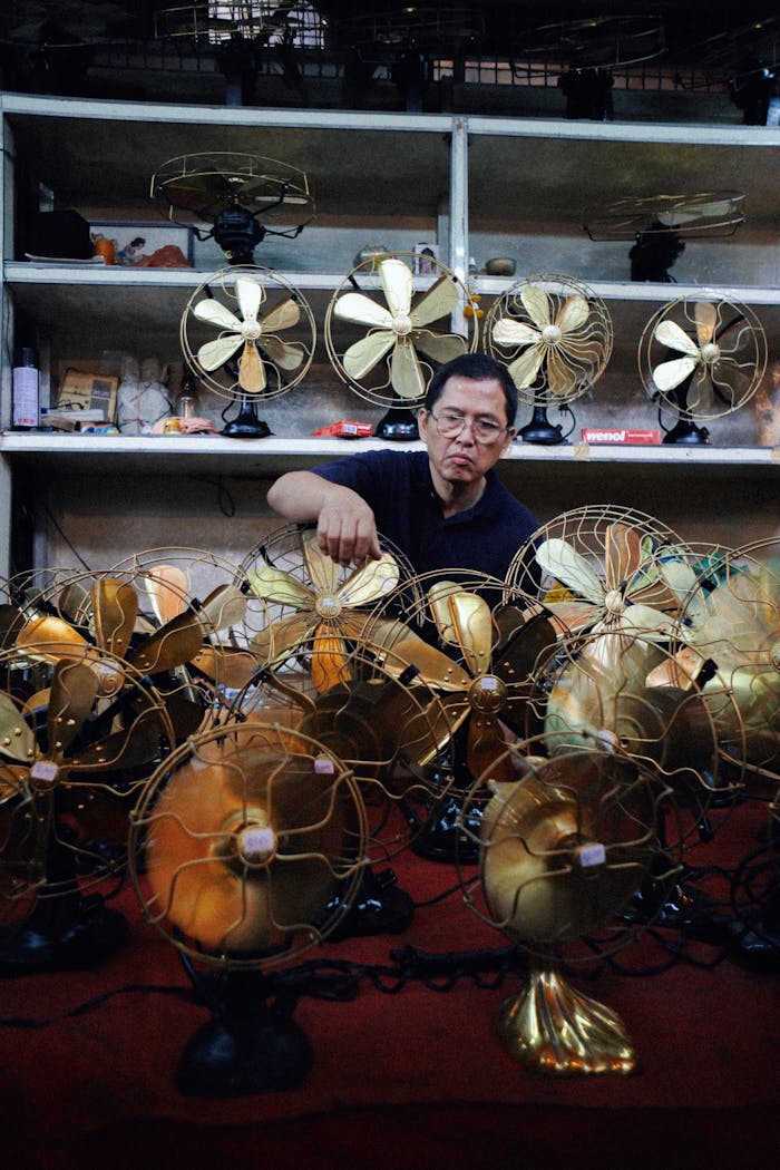 about-01 Man organizes vintage fans at an indoor antique shop stand, showcasing retro merchandise.